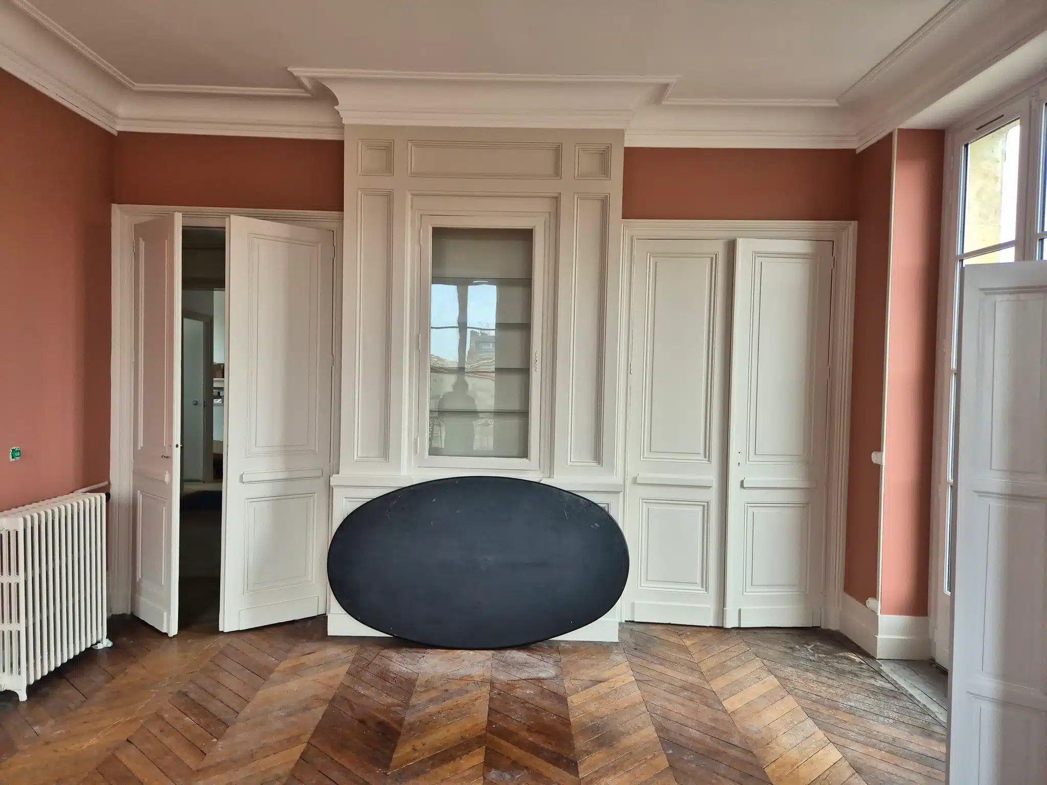 Salon haussmannien repeint en terracotta avec boiseries blanches et parquet en point de Hongrie