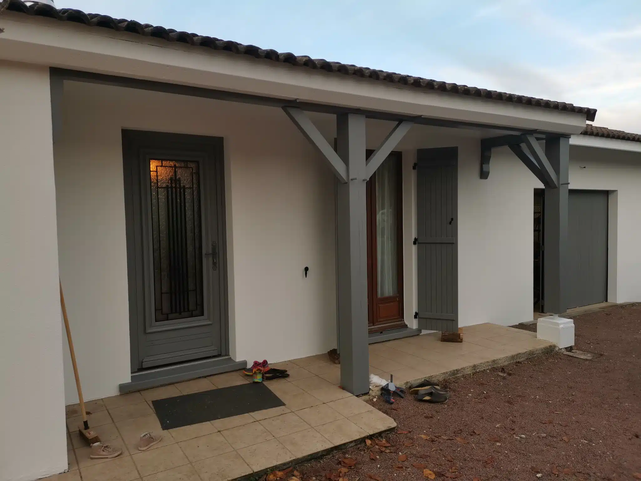 Entrée de maison après travaux : façade blanche, porte, volets et poteaux peints en gris