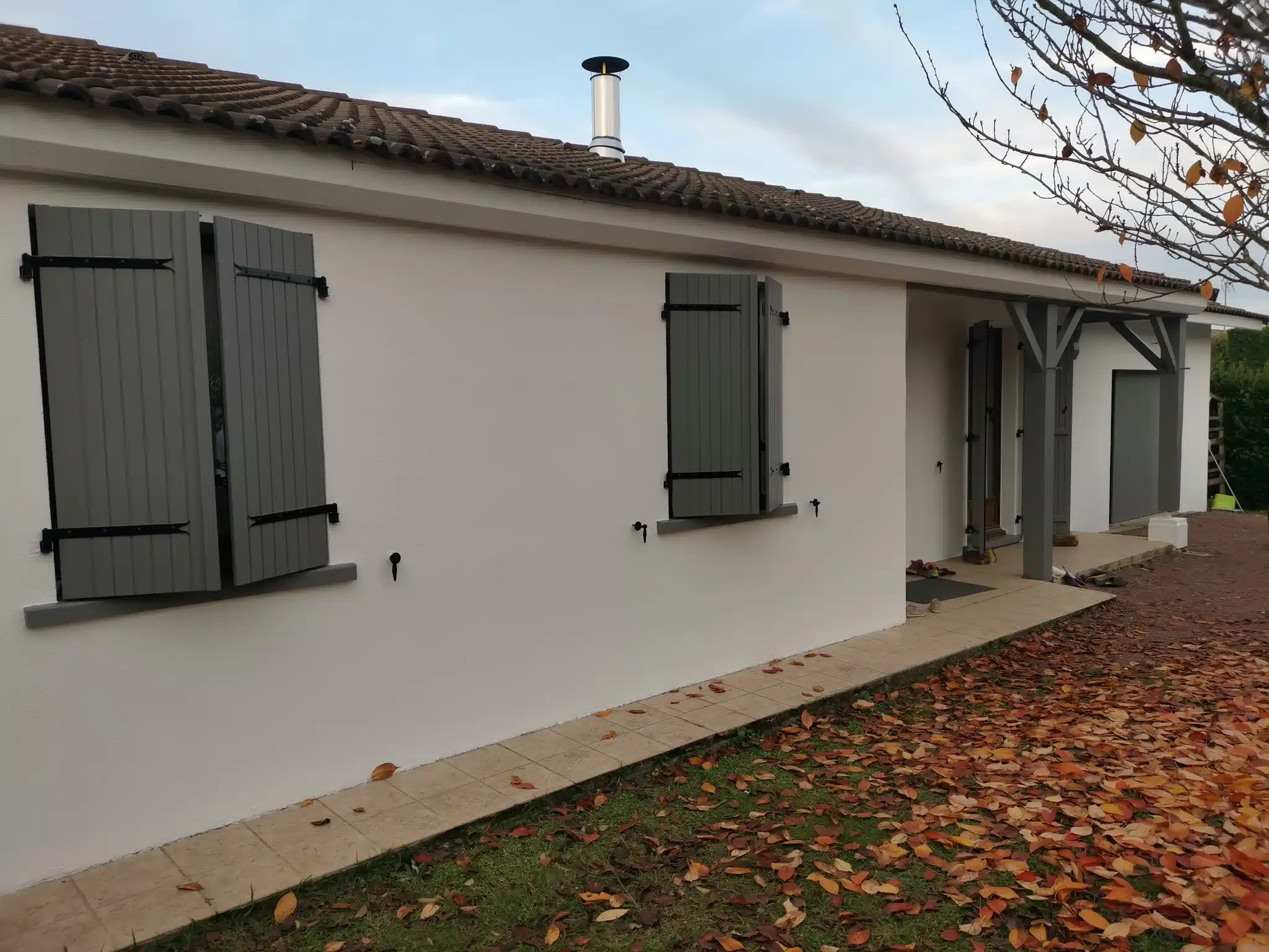 Façade de maison repeinte en blanc avec volets gris ardoise